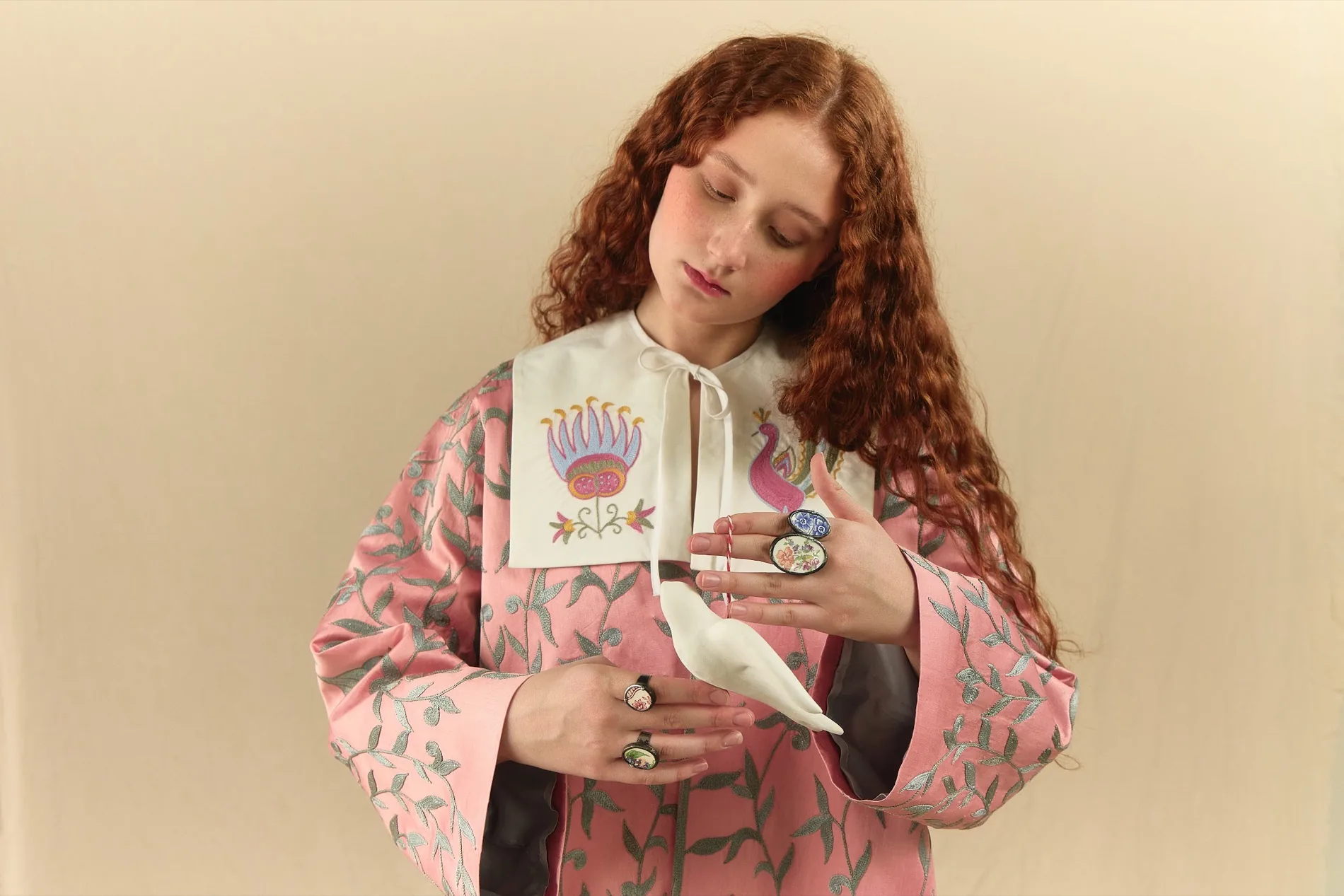 Model in a Suzani-embroidered robe with hand-painted ceramic rings, holding a porcelain bird